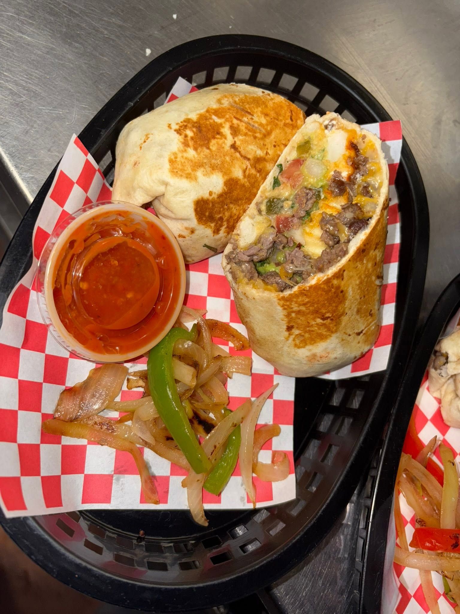 A sliced steak burrito in a basket with salsa and grilled onions