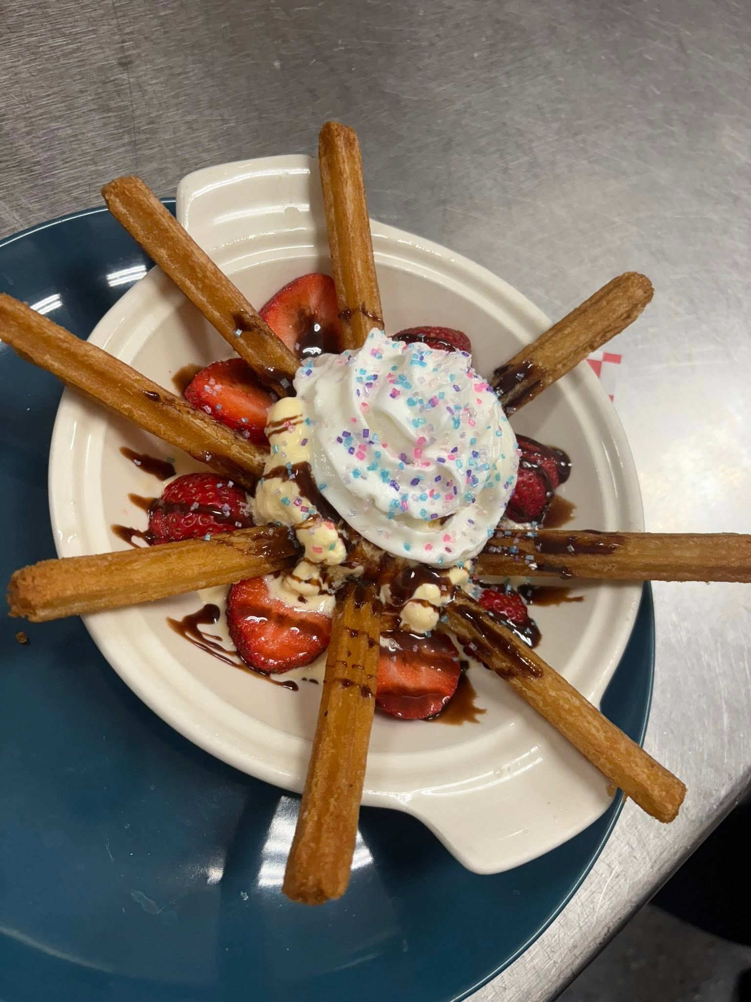 Churros fanned around strawberries and whipped cream with a chocolate drizzle