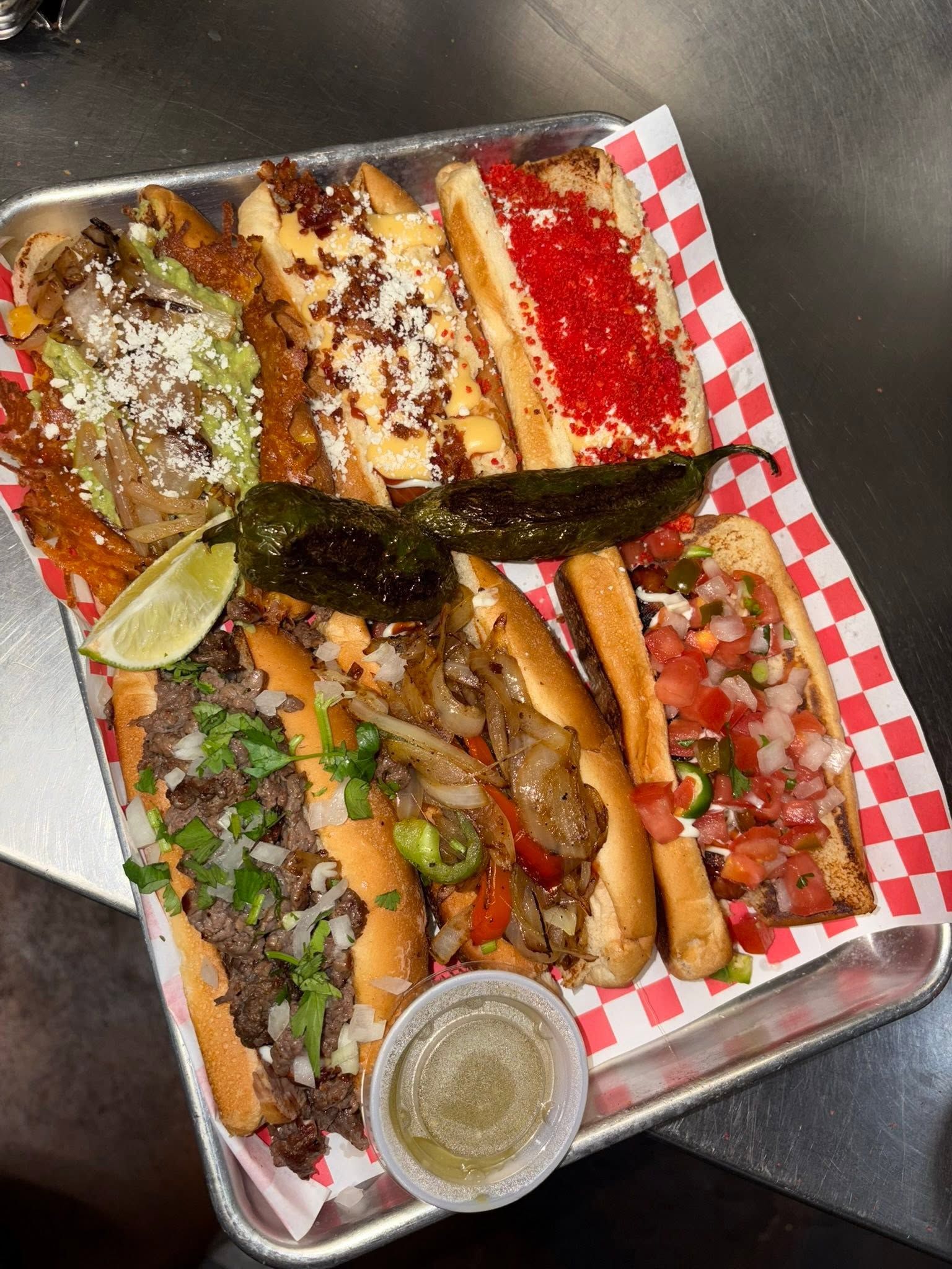 A tray of six dogos with guacamole, Hot Cheetos and pico, roasted jalapeños and limes