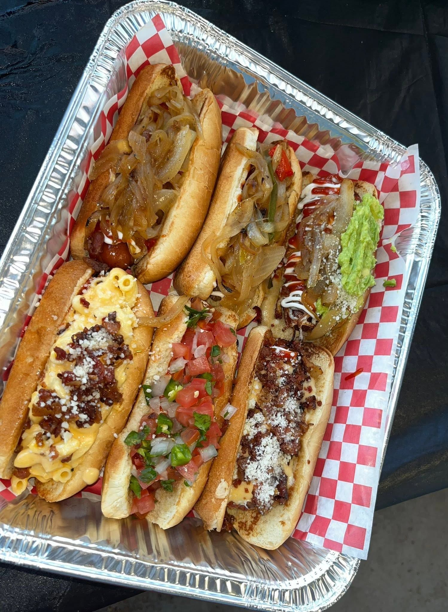 Foil tray of mixed dogo varieties with grilled onion, mac and cheese bacon, and guacamole toppings