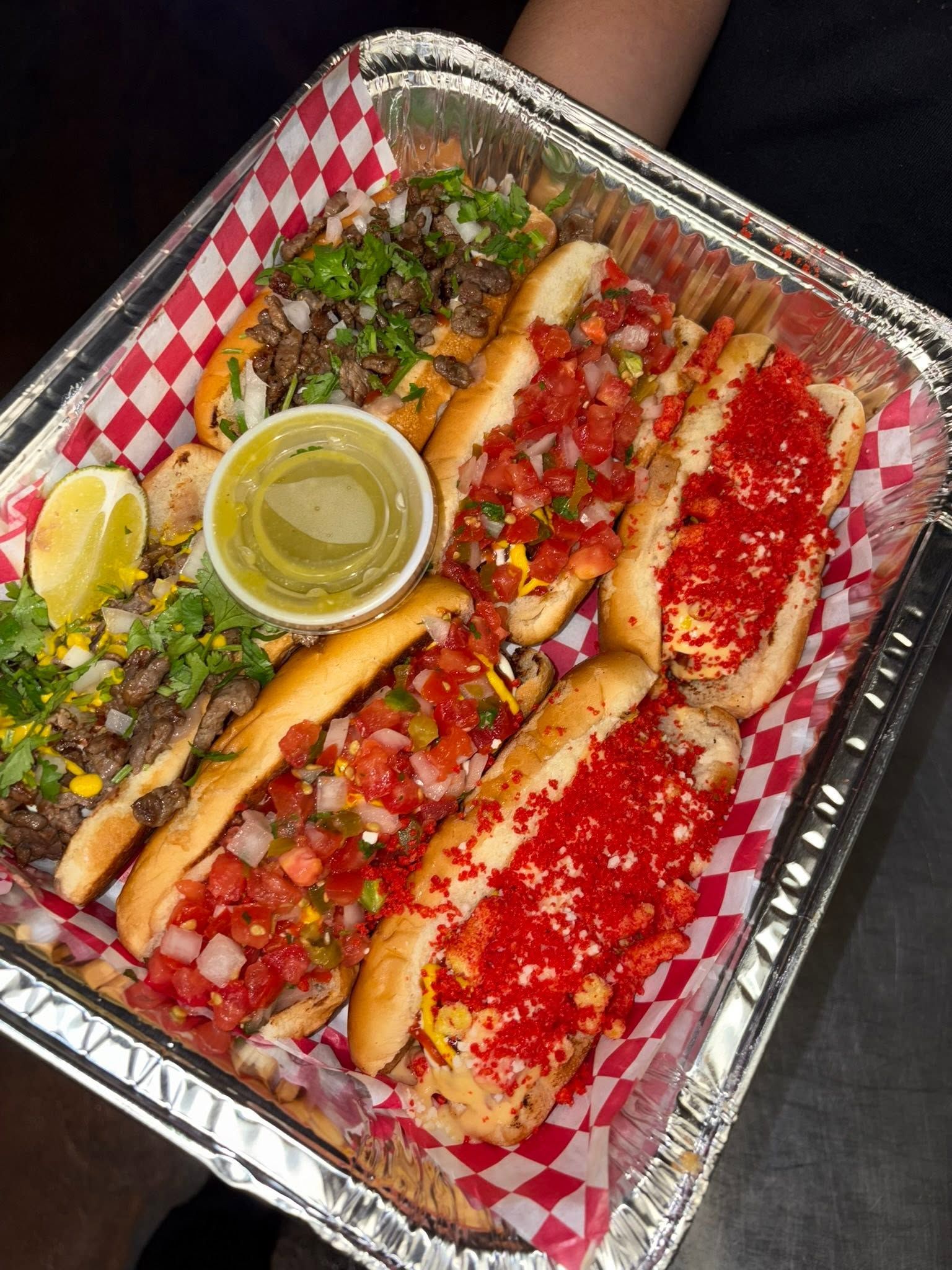 Hand holding a tray of dogos topped with hot cheeto crumbs, pico de gallo, and carne asada