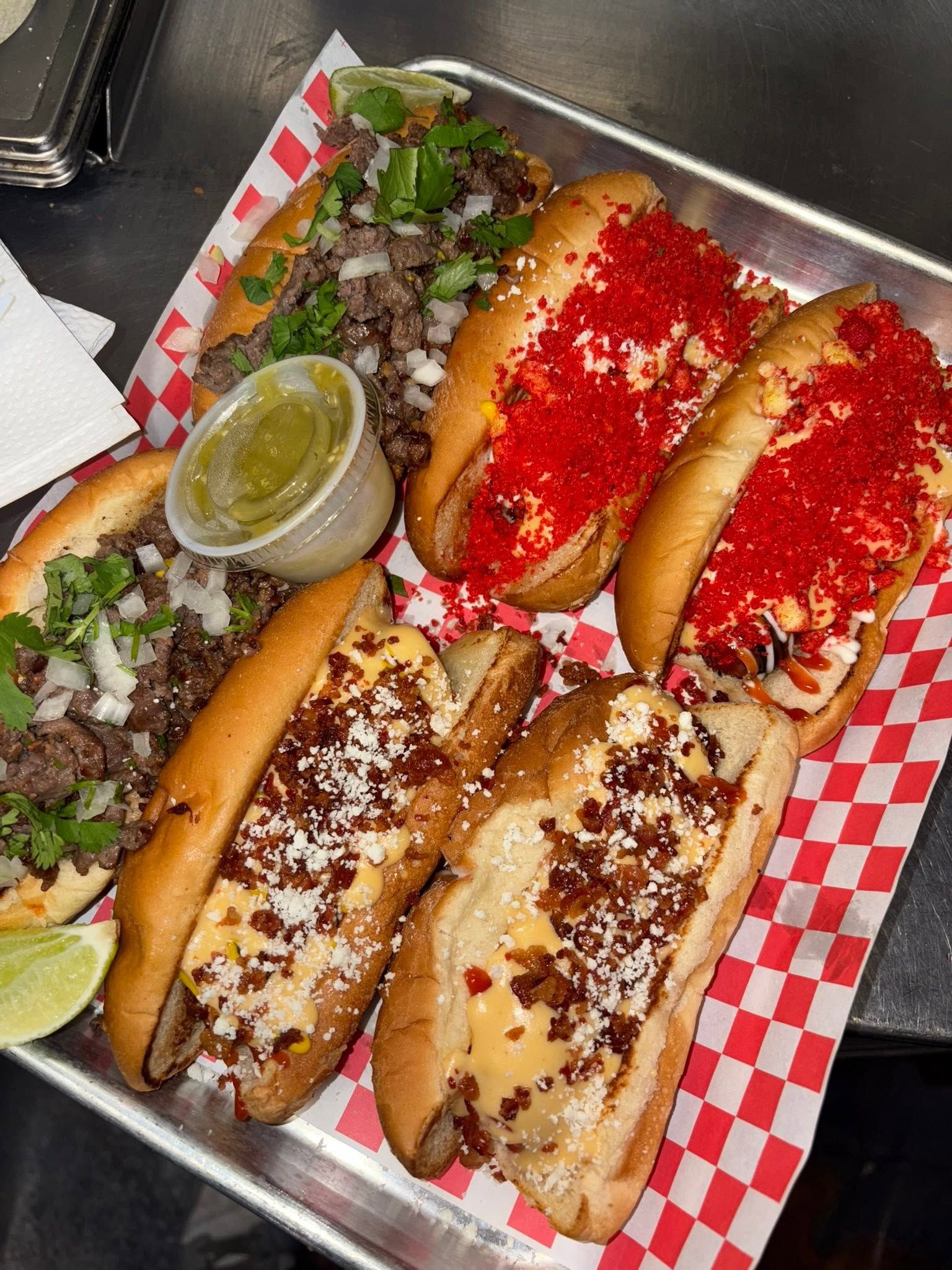 Dogos topped with hot cheeto crumbs and mac and cheese bacon, served with salsa verde and lime