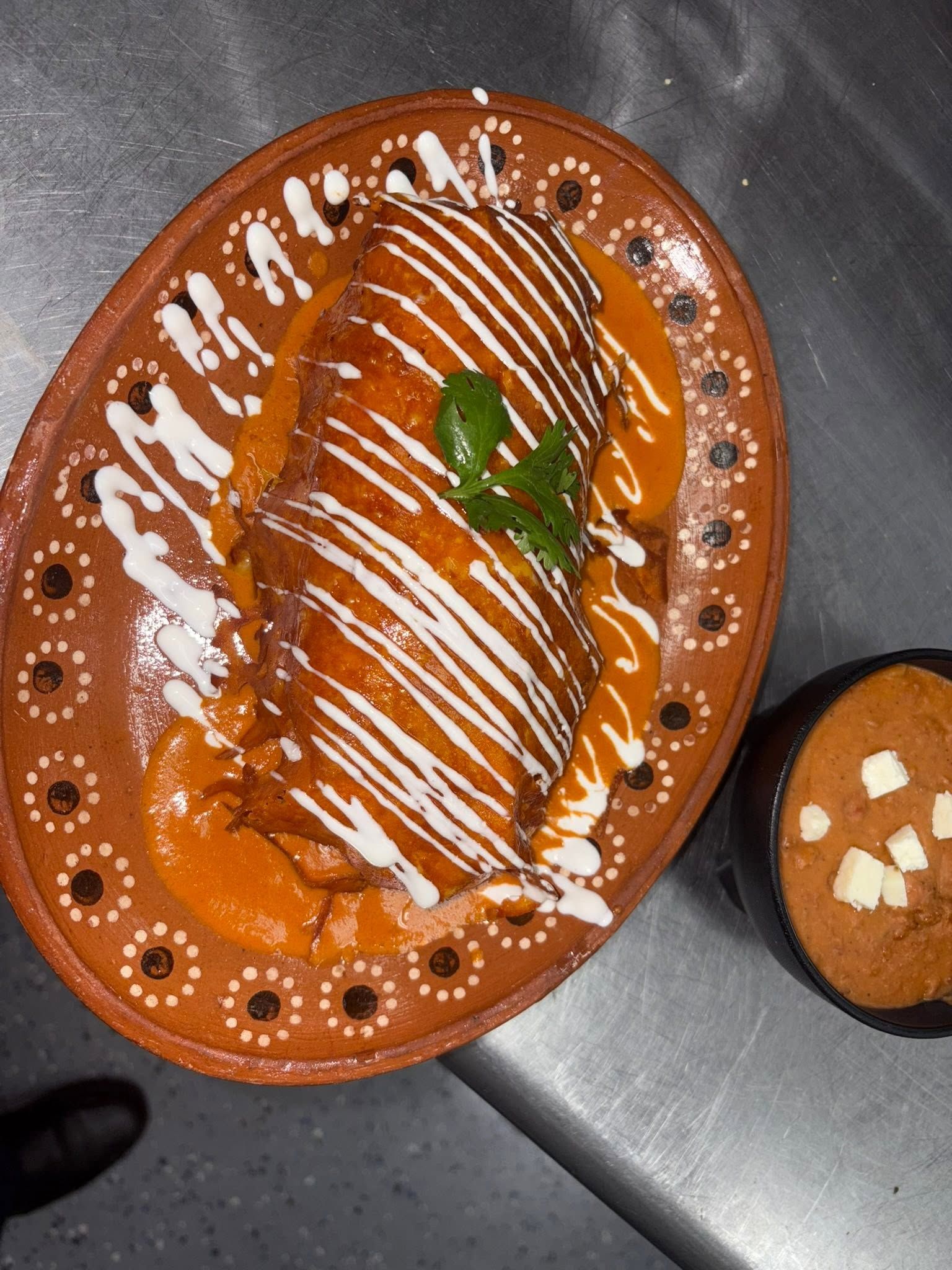 Rolled enchilada in orange chile sauce with crema drizzle and cilantro, side of bean soup