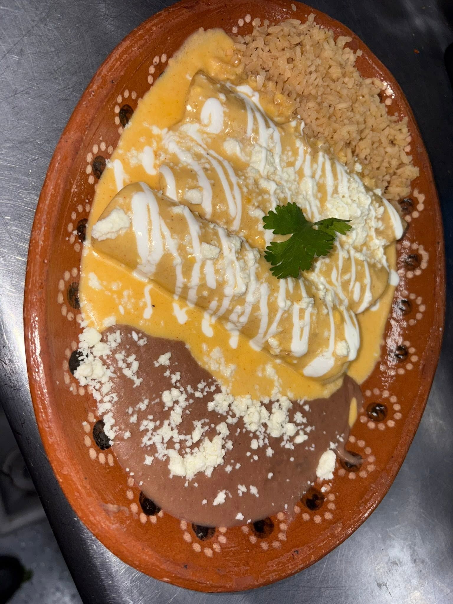 Cheese enchiladas topped with queso sauce, crema and cotija, with rice and refried beans