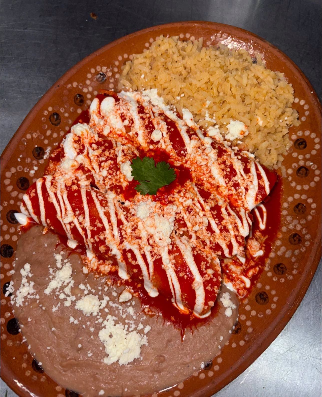 Red enchiladas striped with crema and cotija, with rice and refried beans