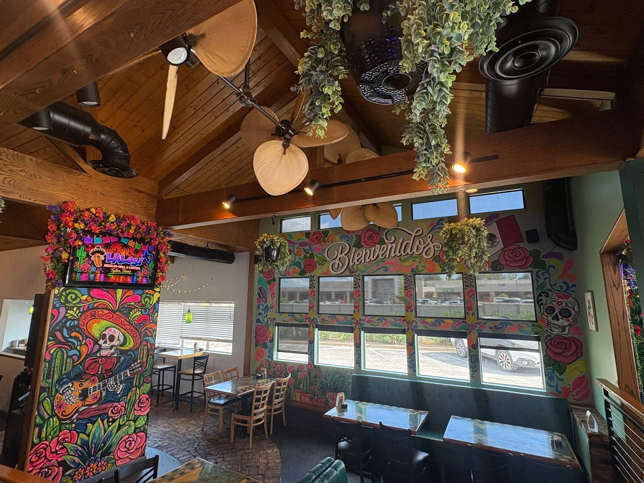 The dining room: a wood ceiling with palm-leaf fans, hanging plants and a Bienvenidos mural of roses around the windows