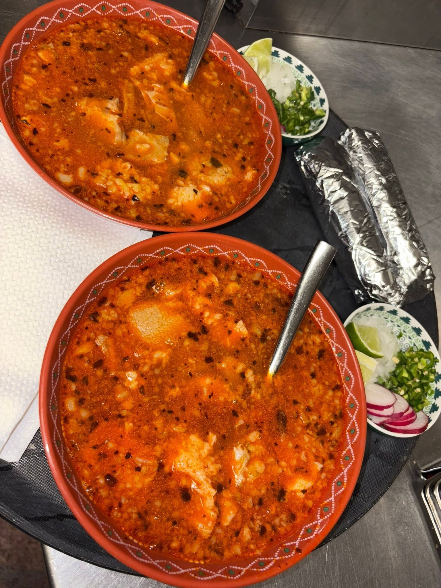Two bowls of red menudo with onion, jalapeño and tortillas
