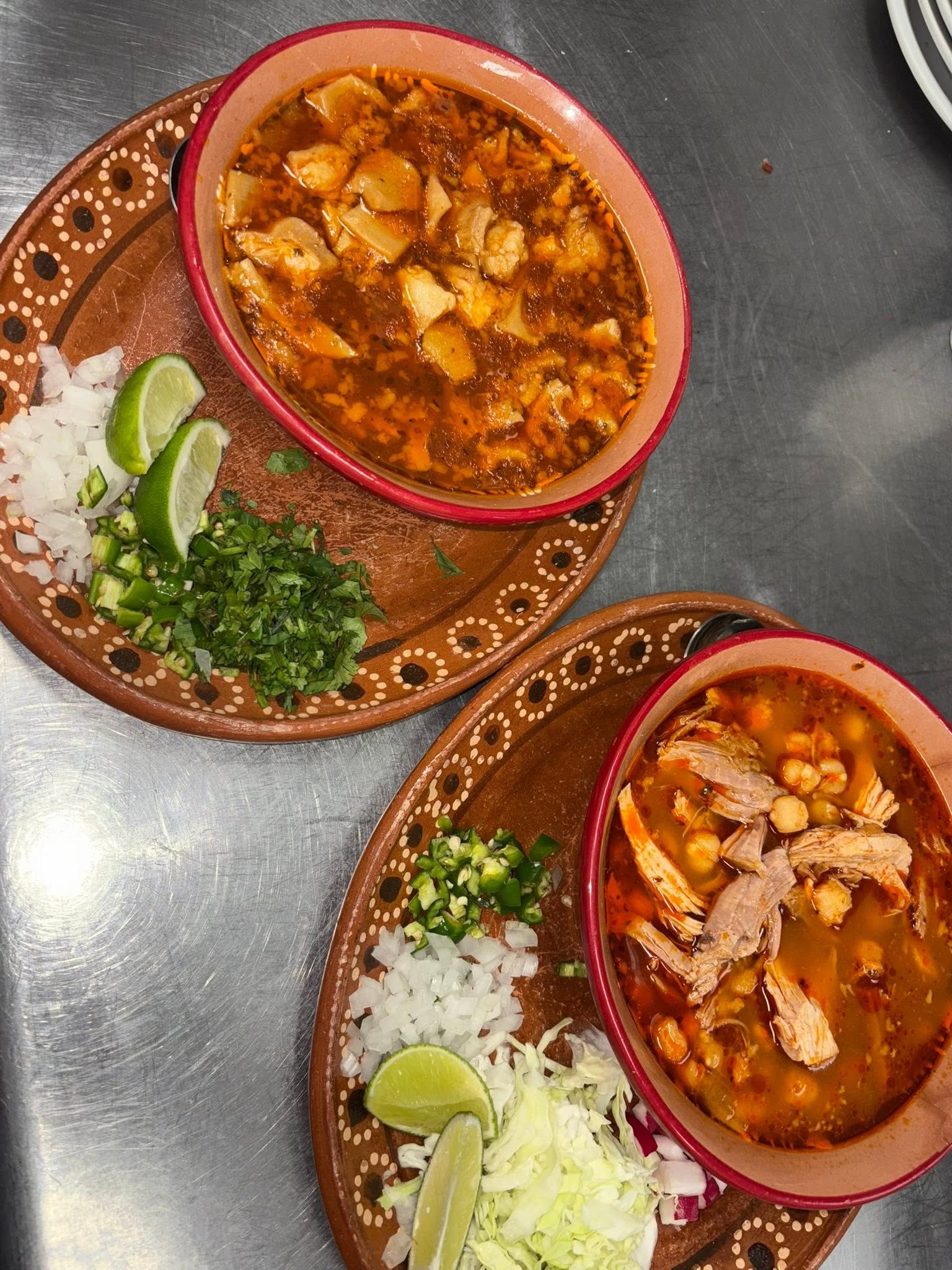 Bowls of red menudo and pozole with lime, onion, cilantro and cabbage