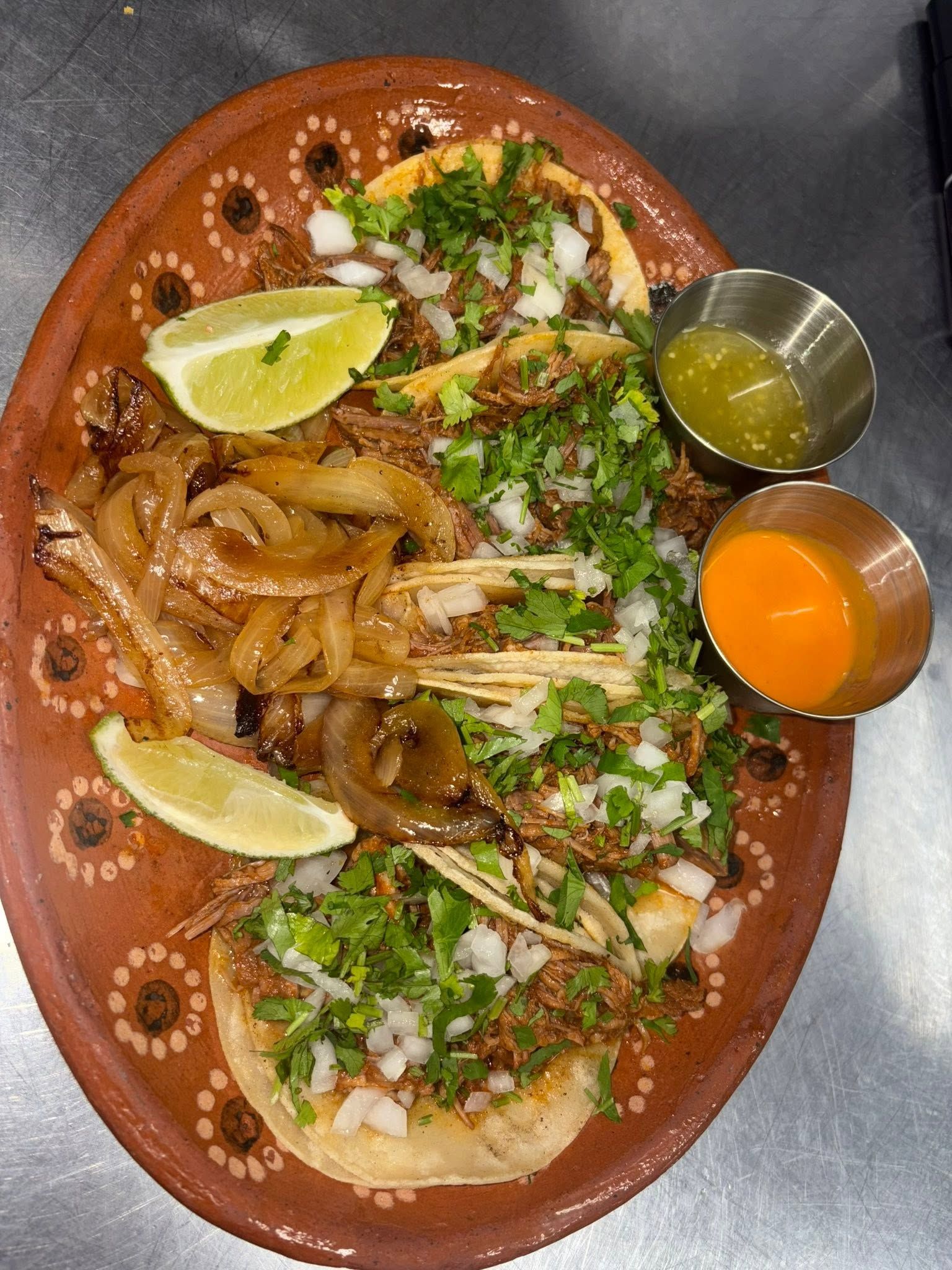 Birria-style shredded beef tacos with onion, cilantro, and dipping consommé