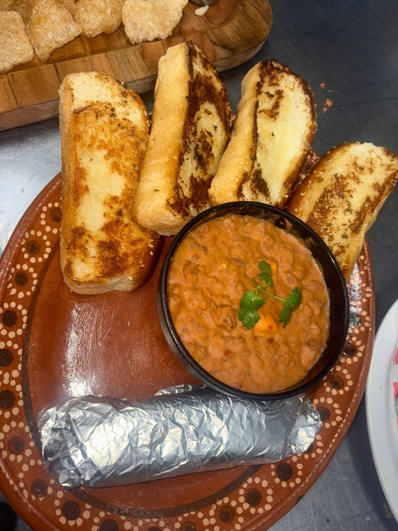 Toasted garlic bread with a bowl of beans and a foil-wrapped burrito