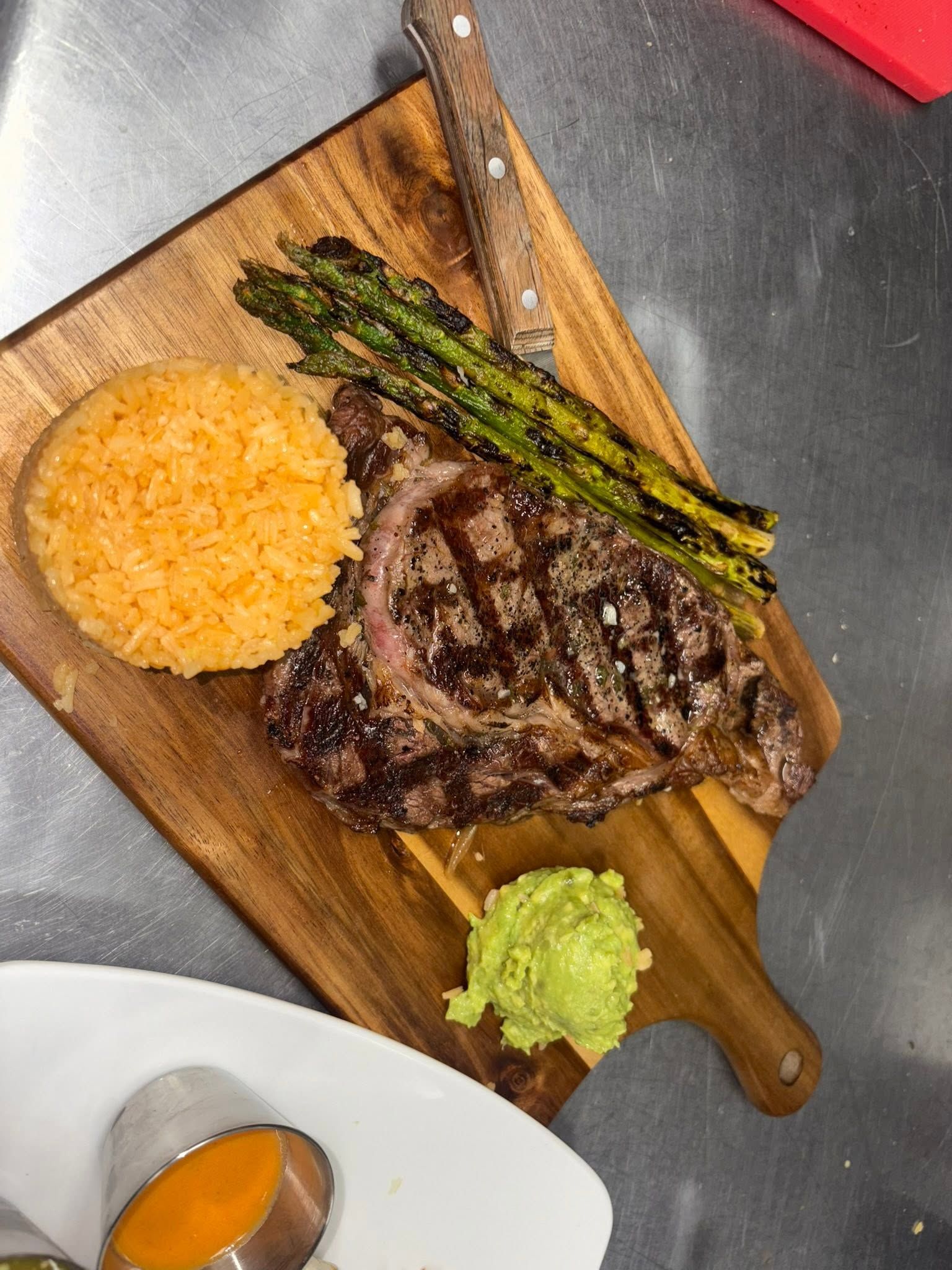 Grilled ribeye on a wooden board with orange rice, charred asparagus and guacamole