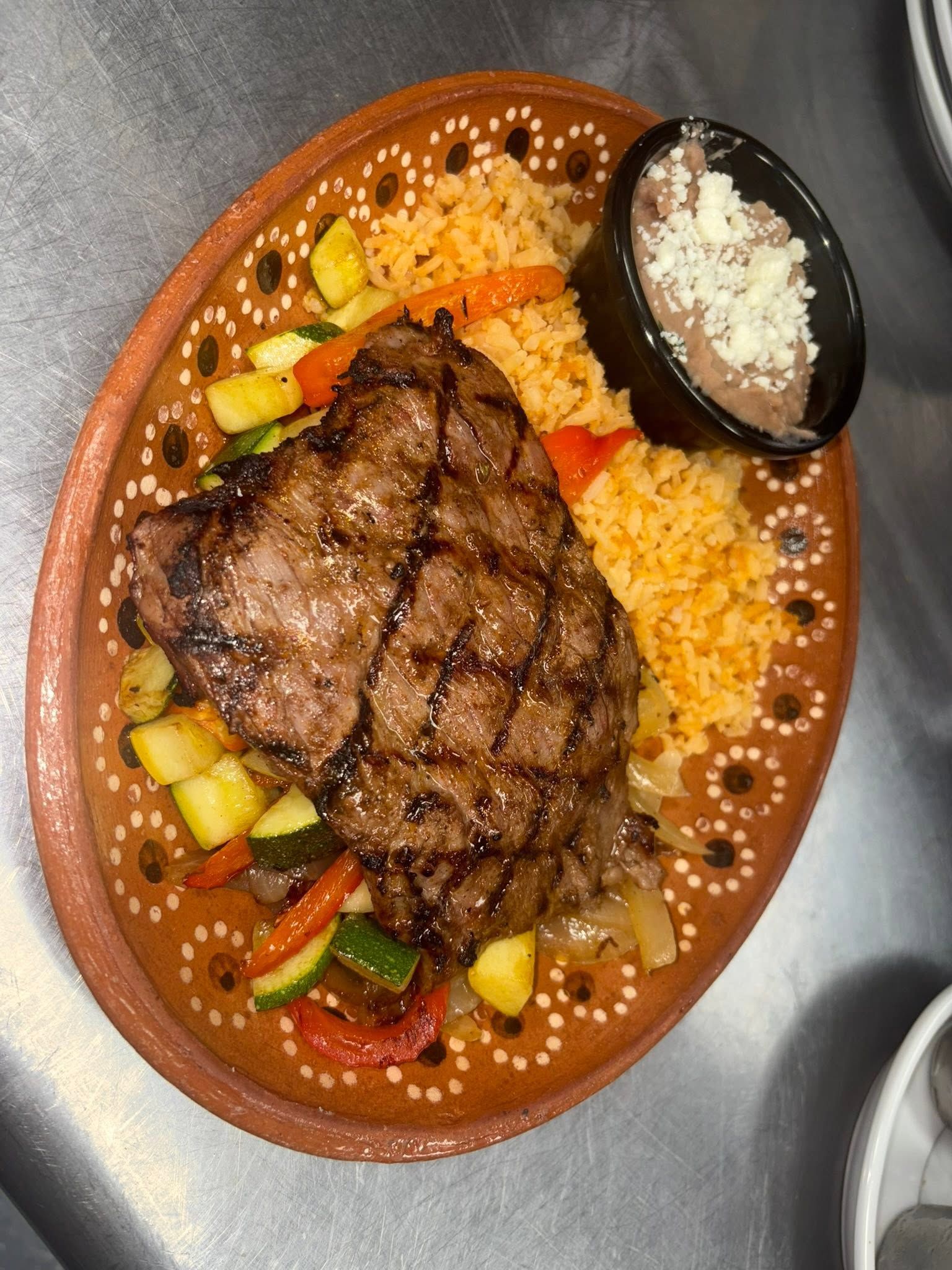 Grilled ribeye on a barro plate with orange rice and grilled vegetables