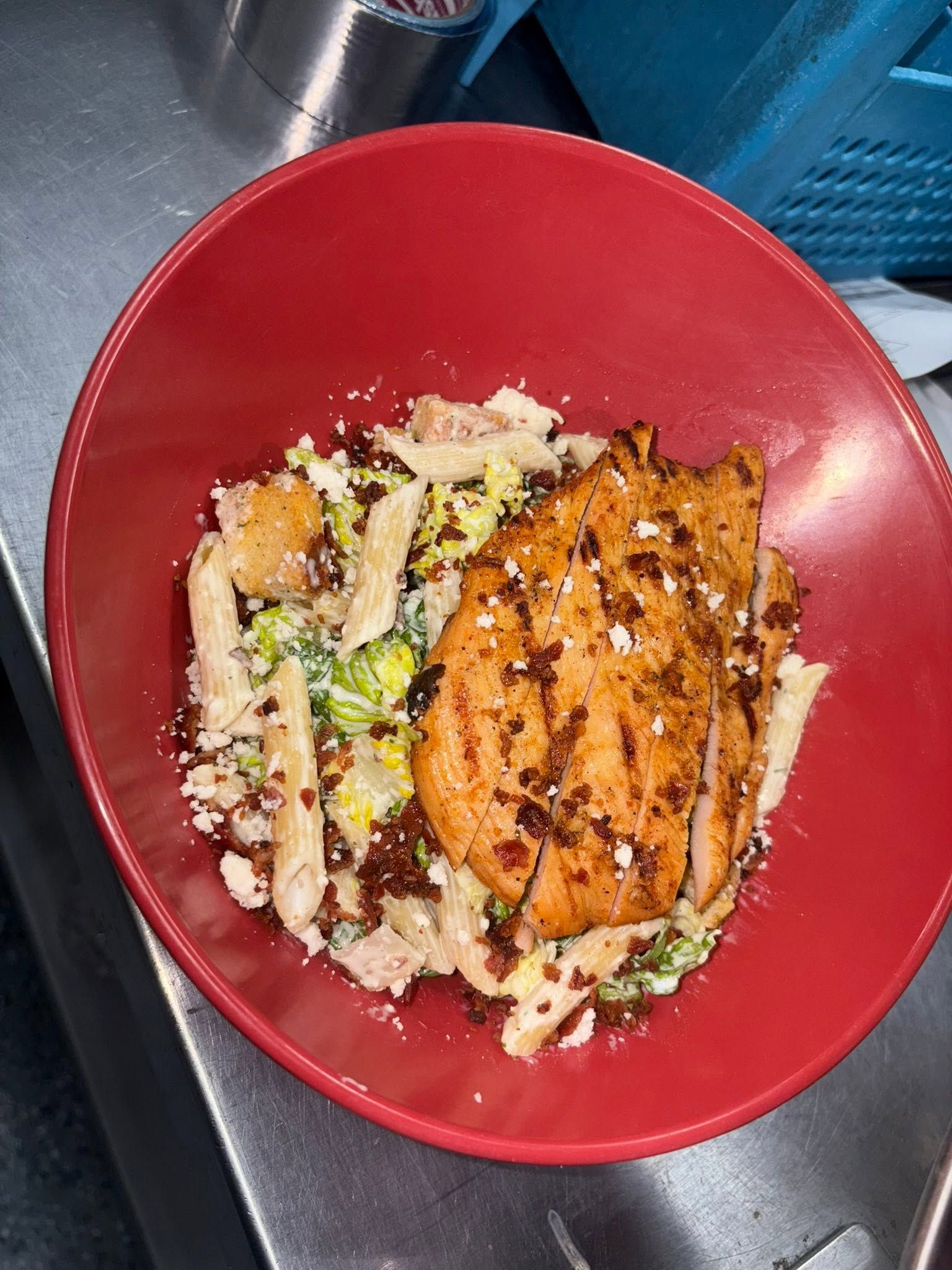 Blackened salmon fillet over Caesar pasta salad with bacon bits and cotija cheese