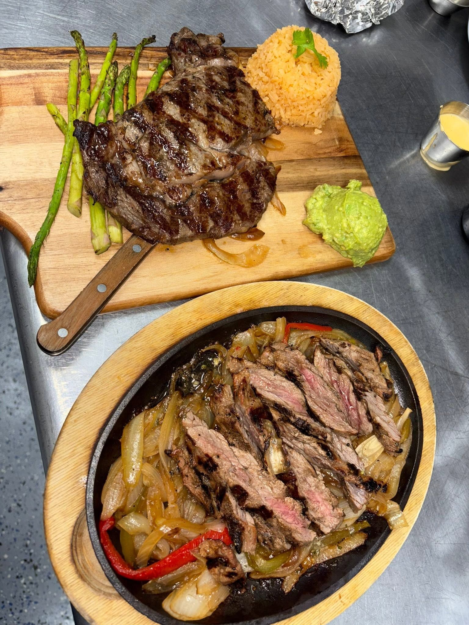A steak with asparagus on a board next to a sizzling fajita skillet