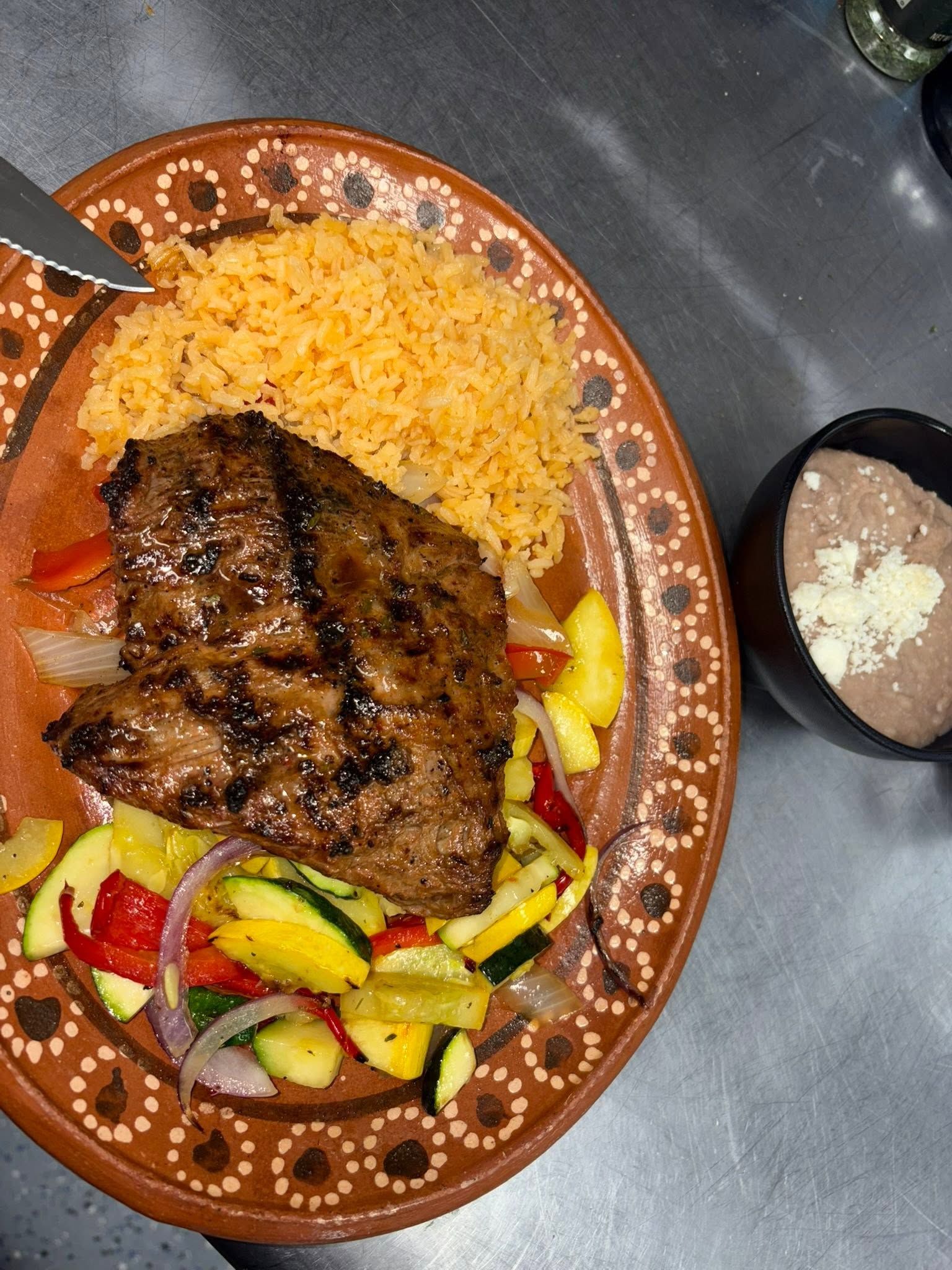 Grilled steak plate with Mexican rice, roasted vegetables, and a side of refried beans
