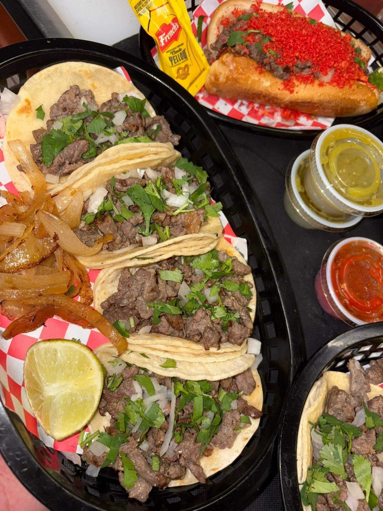 A basket of street tacos with onion, cilantro and lime beside a loaded dogo
