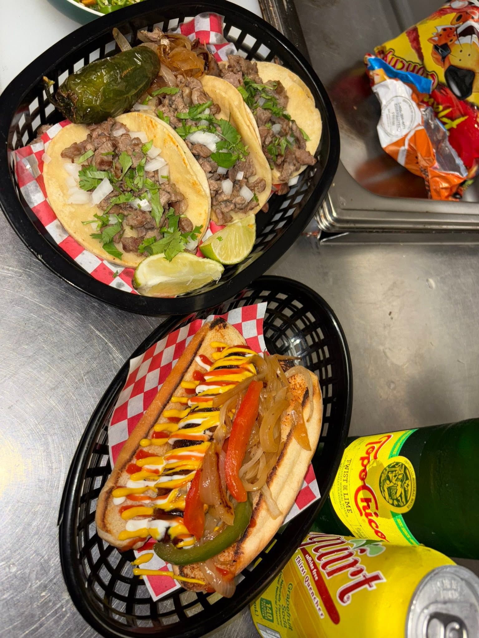 Street tacos with grilled jalapeño beside a bacon-wrapped dogo topped with peppers and onions